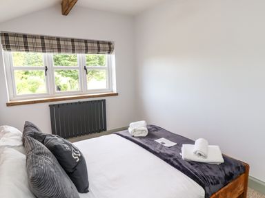 A bedroom with a bed with pillows and folded towels near a window with a radiator below at Holida Hoose in Belford