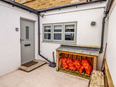 An outdoor area with a gray door a doormat a window and a wood storage unit containing bags of orange firewood at Holida Hoose in Belford