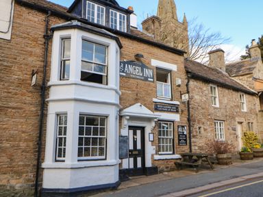 The exterior of a brick building with signs for The Angel Inn a pub with a beer garden and car park at rear in Alston