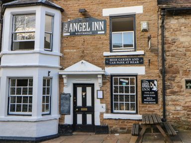 The exterior of The Angel Inn with windows, signs, a black and white door, and a wooden picnic table at 1 The Stables in Alston