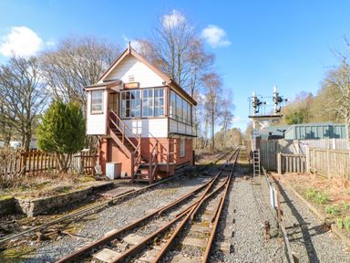 Railway signal box building next to train tracks with trees and fencing at 1 The Stables in Alston
