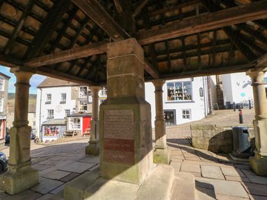 Stone pillars supporting a roof structure in a market square with shops and buildings in the background at 1 The Stables in Alston