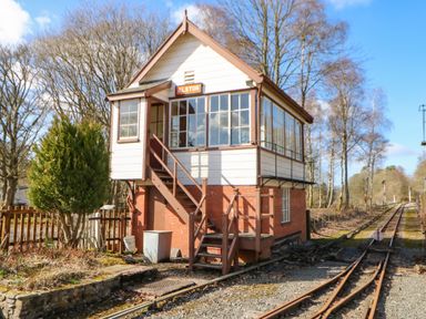 A two-story signal box building next to railway tracks surrounded by trees at 1 The Stables in Alston