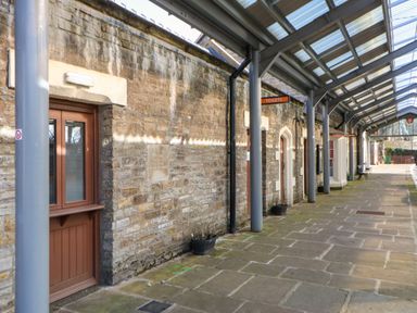 An outdoor walkway with a covered roof next to stone walls with wooden doors and signs for toilets and ticket office at 1 The Stables in Alston