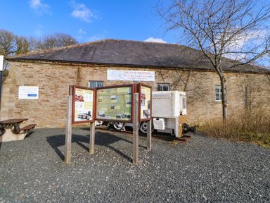 An outdoor display with informational boards and a small white locomotive in front of a stone building at 1 The Stables in Alston