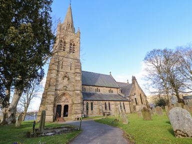 A stone church with a tall steeple and surrounding gravestones at 1 The Stables in Alston