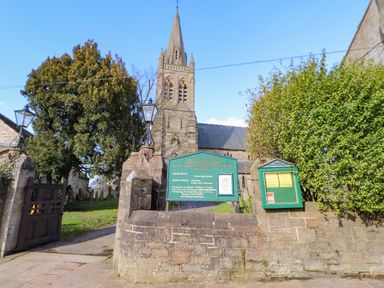 An entrance to a church with a stone wall and a green sign in front of the church at 1 The Stables in Alston