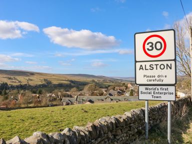 A road sign indicating 30 speed limit and Alston town with houses and hills in the background at 1 The Stables in Alston