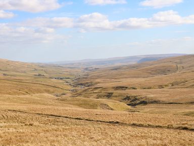 A wide view of rolling fields and hills under a blue sky with scattered clouds at 1 The Stables in Alston