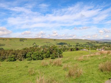 A landscape of green fields with scattered trees and houses under a partly cloudy sky at 1 The Stables in Alston