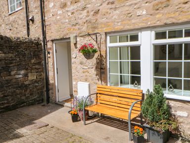 An outdoor area with a wooden bench and potted plants against a stone wall near a door and windows at 1 The Stables in Alston