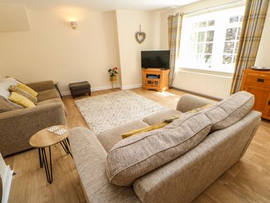 A living room with sofas a television on a wooden stand a rug and a window with curtains at 1 The Stables in Alston