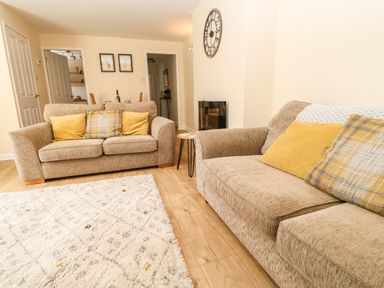 A living room with two beige sofas and yellow cushions a small side table and wall clock at 1 The Stables in Alston