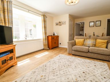 A living room with a beige sofa a wooden cabinet a television a white patterned rug and yellow plaid curtains at 1 The Stables in Alston