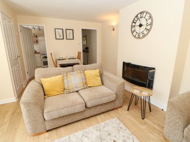 A living room with a sofa yellow cushions a wall clock and a small table at 1 The Stables in Alston
