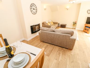 A living area with two beige sofas a dining table set with plates and a bottle a wall clock and a television at 1 The Stables in Alston