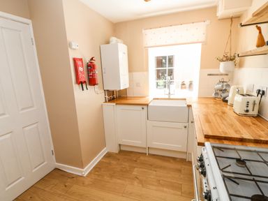 A kitchen with wooden countertops white cabinets a gas stove a sink a toaster a kettle a fire extinguisher and a window at 1 The Stables in Alston