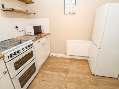 A kitchen with a stove microwave refrigerator wooden shelves and radiator at 1 The Stables Alston