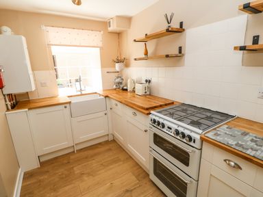 A kitchen with wooden countertops white cabinets a white stove a farmhouse sink and wooden shelves at 1 The Stables in Alston