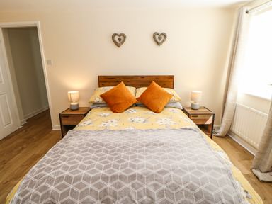 A bedroom with a double bed with floral bedding and two orange pillows two bedside tables with lamps wooden floor and two heart decorations on the wall at 1 The Stables in Alston
