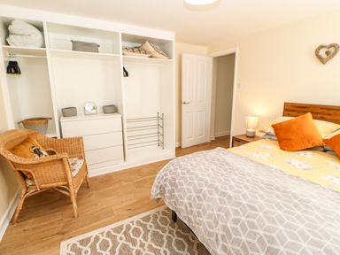 A bedroom with a bed with yellow and orange pillows a wicker chair an open white closet and a wooden floor at 1 The Stables in Alston