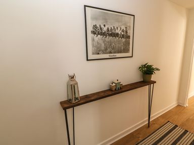 A hallway with a narrow wooden console table holding a lantern a small house decoration and a potted plant with a black and white photo on the wall above at 1 The Stables in Alston