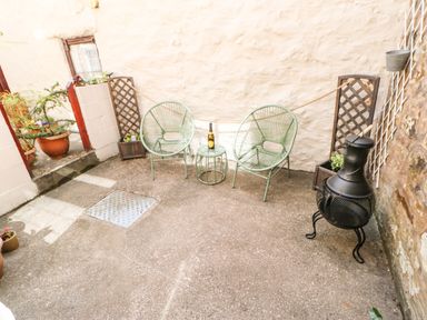 An outdoor patio with two green chairs a small table with a bottle two trellises and a black chiminea at 1 The Stables in Alston