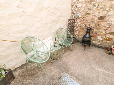 A small outdoor patio with two green chairs a matching table with a bottle and glass on top a chiminea and potted plants at 1 The Stables in Alston