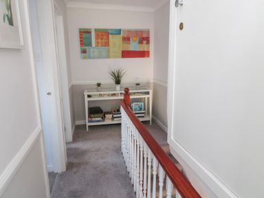 A hallway with a railing and a white console table with plants and books at The Nest in Beadnell