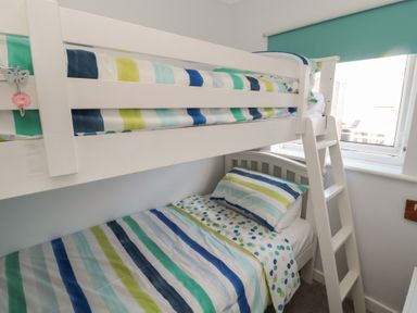 A bedroom with a white bunk bed striped bedding and a window with blinds at The Nest in Beadnell