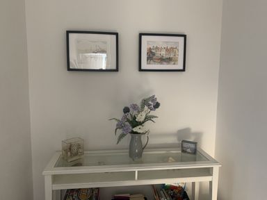 An entryway with photographs on the wall and a table with a vase and books at The Nest in Beadnell