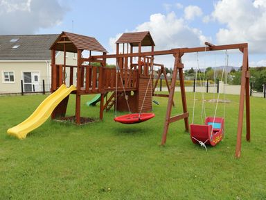A wooden playground with slides and swings on grass at Loughanure Lake View in Loughanure County Donegal