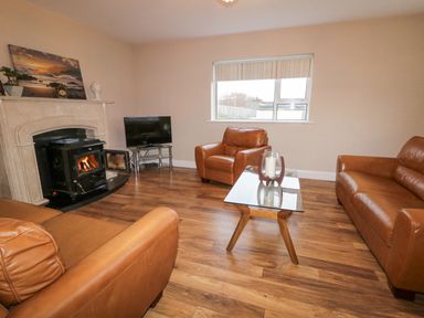 A living room with brown leather sofas a glass coffee table a wood burning stove and a television at Loughanure Lake View in Loughanure County Donegal