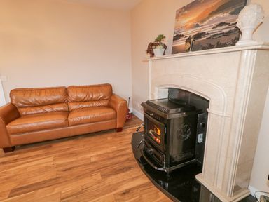 A living room with a brown leather sofa a black stove in a beige marble fireplace and a painting on the mantel at Loughanure Lake View in Loughanure County Donegal