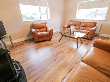 A living room with brown leather sofas a glass coffee table and two windows at Loughanure Lake View in Loughanure County Donegal