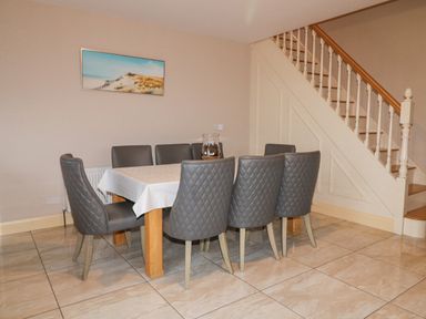 A dining area with a rectangular table covered with a white tablecloth surrounded by eight gray chairs near a staircase at Loughanure Lake View in Loughanure County Donegal