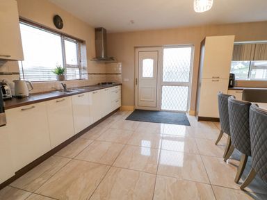 A kitchen with white cabinets a stove a sink a door leading outside and gray chairs at Loughanure Lake View in Loughanure County Donegal