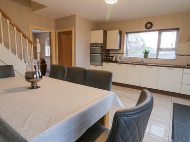 A kitchen and dining area with a table covered with a white cloth and six chairs near cabinets and a window at Loughanure Lake View in Loughanure County Donegal