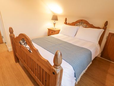A bedroom with a wooden bed with white bedding and a blue throw and a nightstand with a lamp at Loughanure Lake View in Loughanure County Donegal