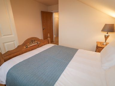 A bedroom with a wooden bed with white bedding and a blue blanket a wooden nightstand with a lamp and an open door at Loughanure Lake View in Loughanure County Donegal