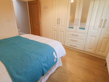 A bedroom with a bed covered by a teal throw and white wardrobe cabinets with mirrored doors at Loughanure Lake View in Loughanure County Donegal