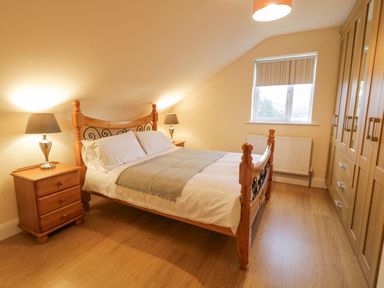A bedroom with a wooden bed and nightstands with lamps and a window at Loughanure Lake View in Loughanure County Donegal