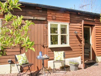 Outdoor seating area with two chairs and a small table in front of a wooden building at The Garden Lodge in Upton Cressett near Bridgnorth