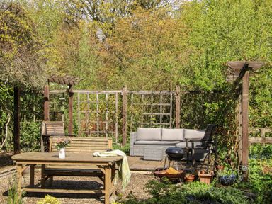 An outdoor garden seating area with wooden table and benches and a patio with sofa and chairs at The Garden Lodge in Upton Cressett near Bridgnorth