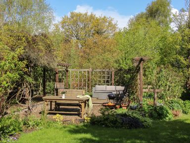 A garden seating area with wooden benches and a table surrounded by plants and trees at The Garden Lodge in Upton Cressett near Bridgnorth