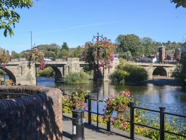 A stone bridge over a river with hanging flower baskets and railings at The Garden Lodge in Upton Cressett near Bridgnorth
