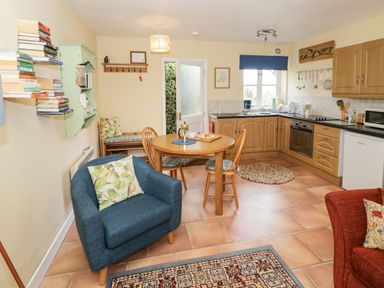 A kitchen and dining area with wooden cabinets a round wooden table four chairs a blue armchair and a red armchair at The Garden Lodge in Upton Cressett near Bridgnorth