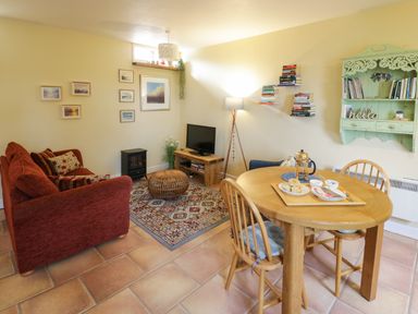 A sitting and dining area with a red sofa a wooden table with chairs a television and wall shelves at The Garden Lodge in Upton Cressett near Bridgnorth