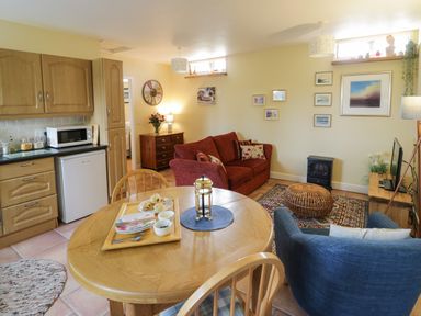 A kitchen and living room with a wooden dining table and chairs a red couch and a blue armchair at The Garden Lodge in Upton Cressett near Bridgnorth