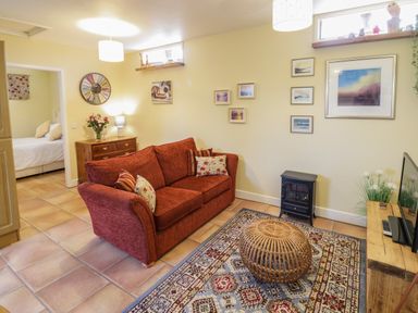 A living room with a red sofa and patterned rug with a wicker coffee table at The Garden Lodge in Upton Cressett near Bridgnorth